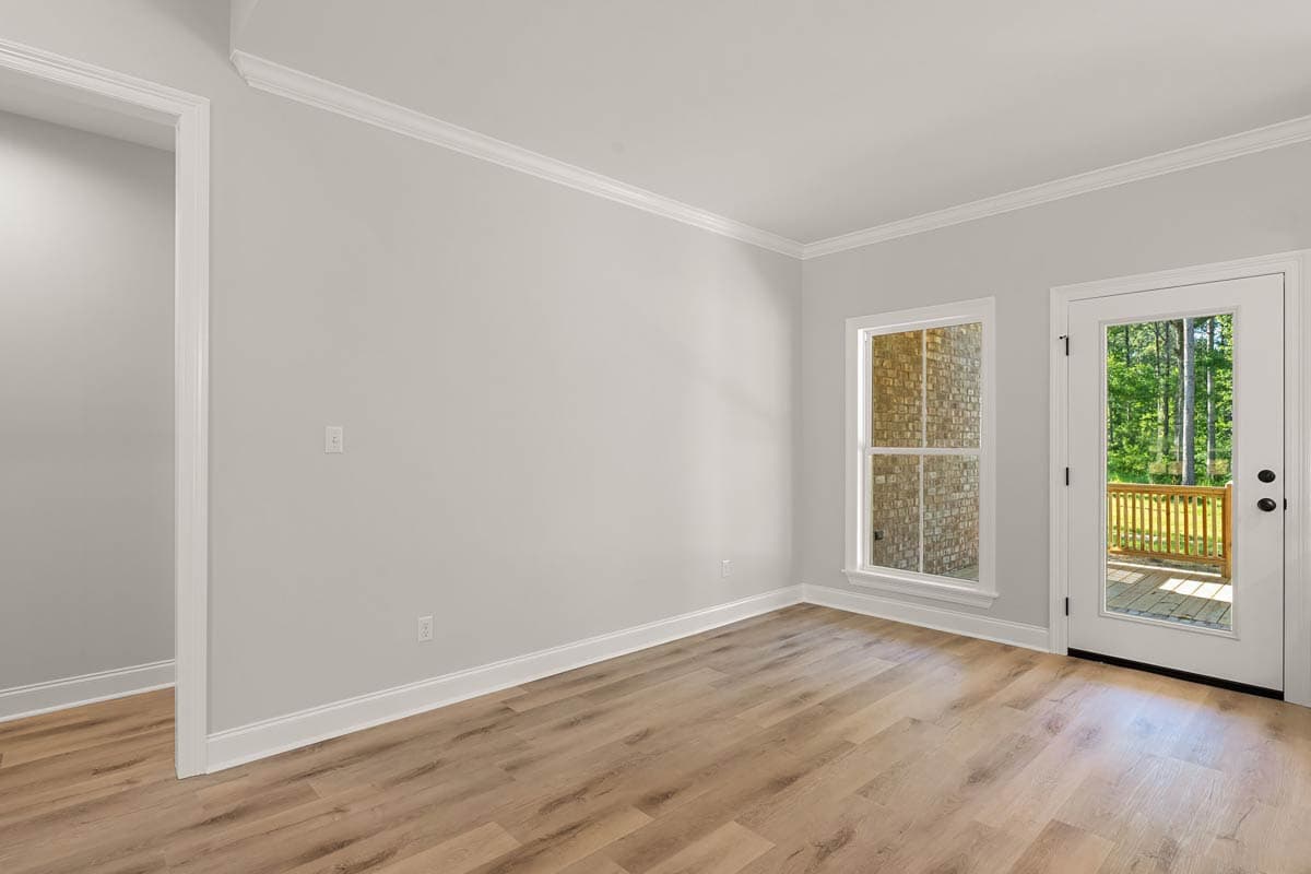 Interior view of room with hardwood floors, a single window showing brick exterior, and a glass door leading to a wooden deck.