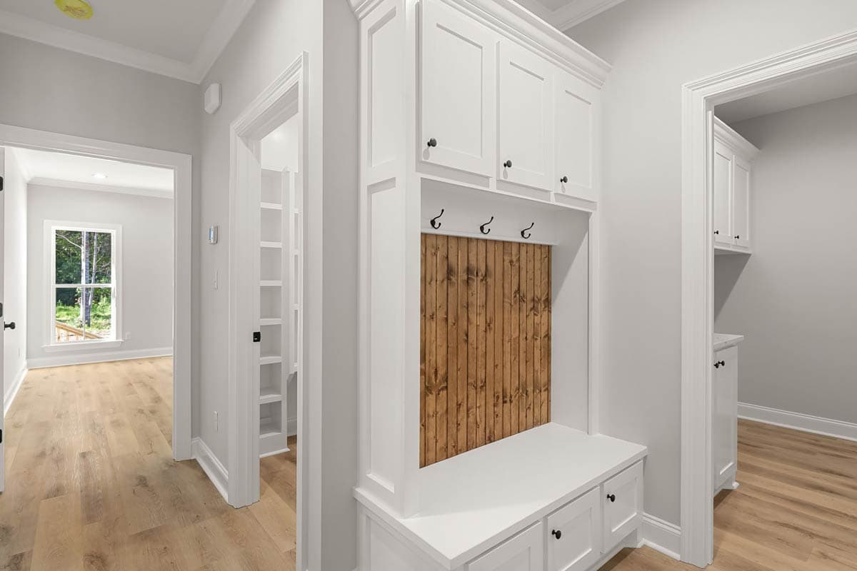 Hallway with built-in white cabinetry, wood-paneled accent wall, bench seating, and entryway to another room with a window.