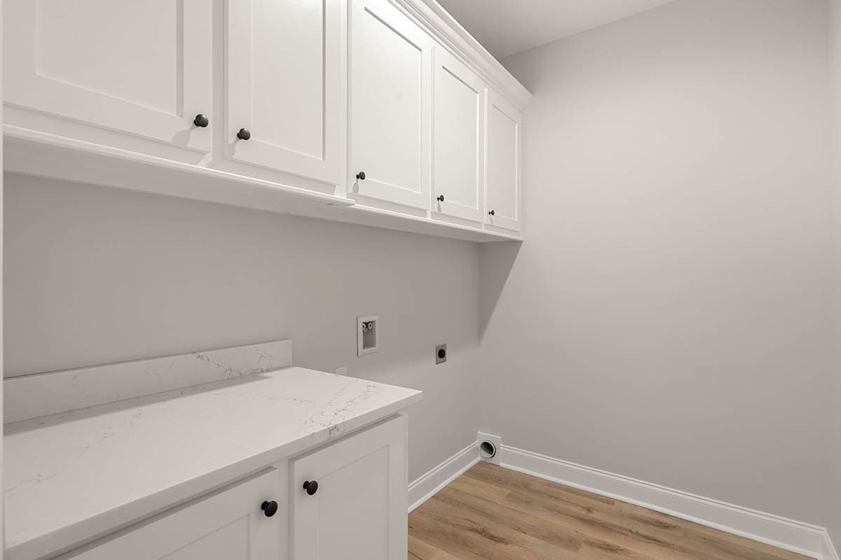 Laundry room interior with white cabinetry, quartz countertop, washer/dryer hookups and vent.
