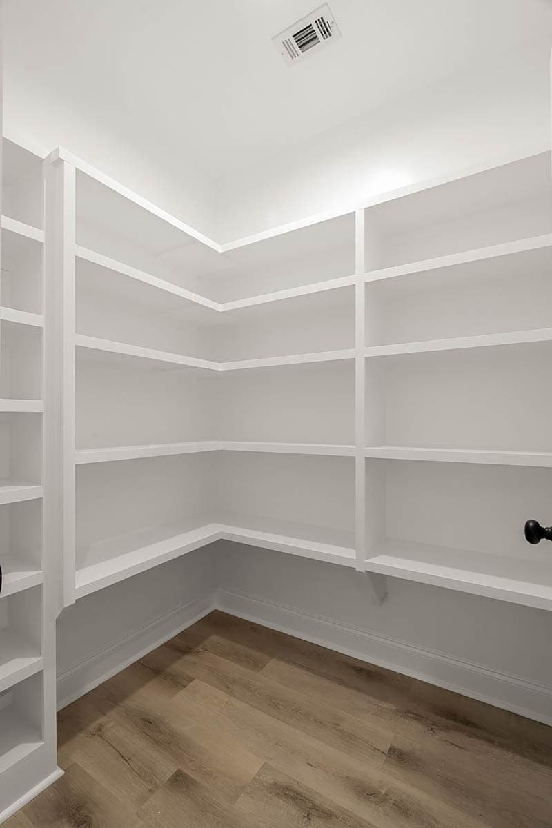 Pantry with white built-in shelves on three walls and wood-look flooring.