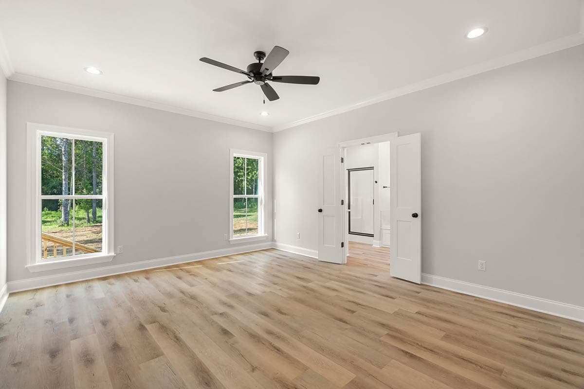 Bedroom interior with two windows, ceiling fan, and double doors opening to a bathroom with a shower.