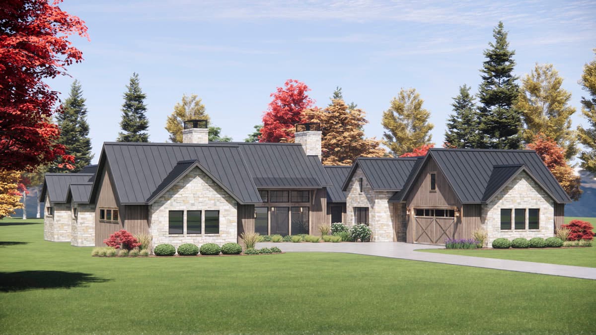 A modern, stone-clad house with a dark metal roof. Tall evergreens and colorful fall trees surround the home, set on a large grassy lawn.