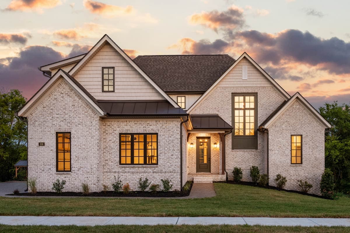 House plan exterior. Two-story, brick facade, gabled roof, and multiple dormers. Features include a covered entry and black window frames.
