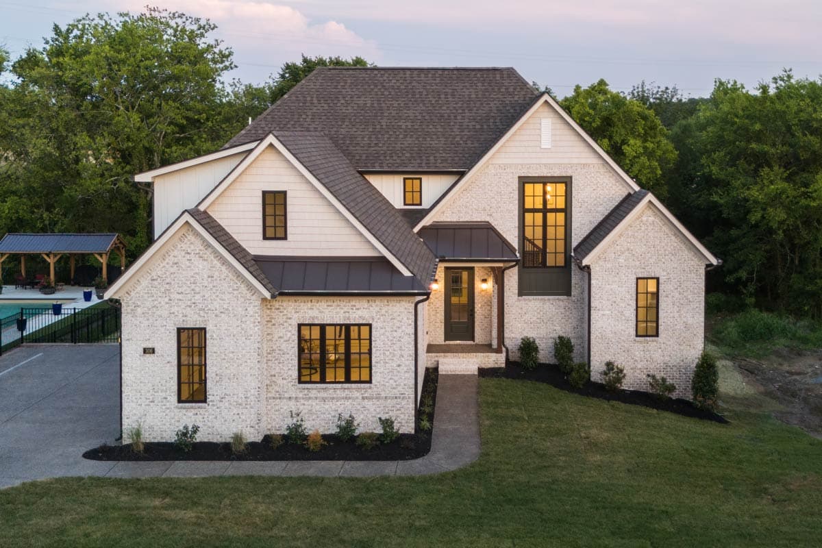 House plan exterior showing a two-story Modern Farmhouse with white brick, metal roof accents, gables, and large windows.
