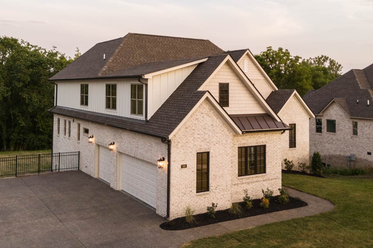 House plan exterior with white brick facade, three-car garage, prominent gables, and board-and-batten siding.