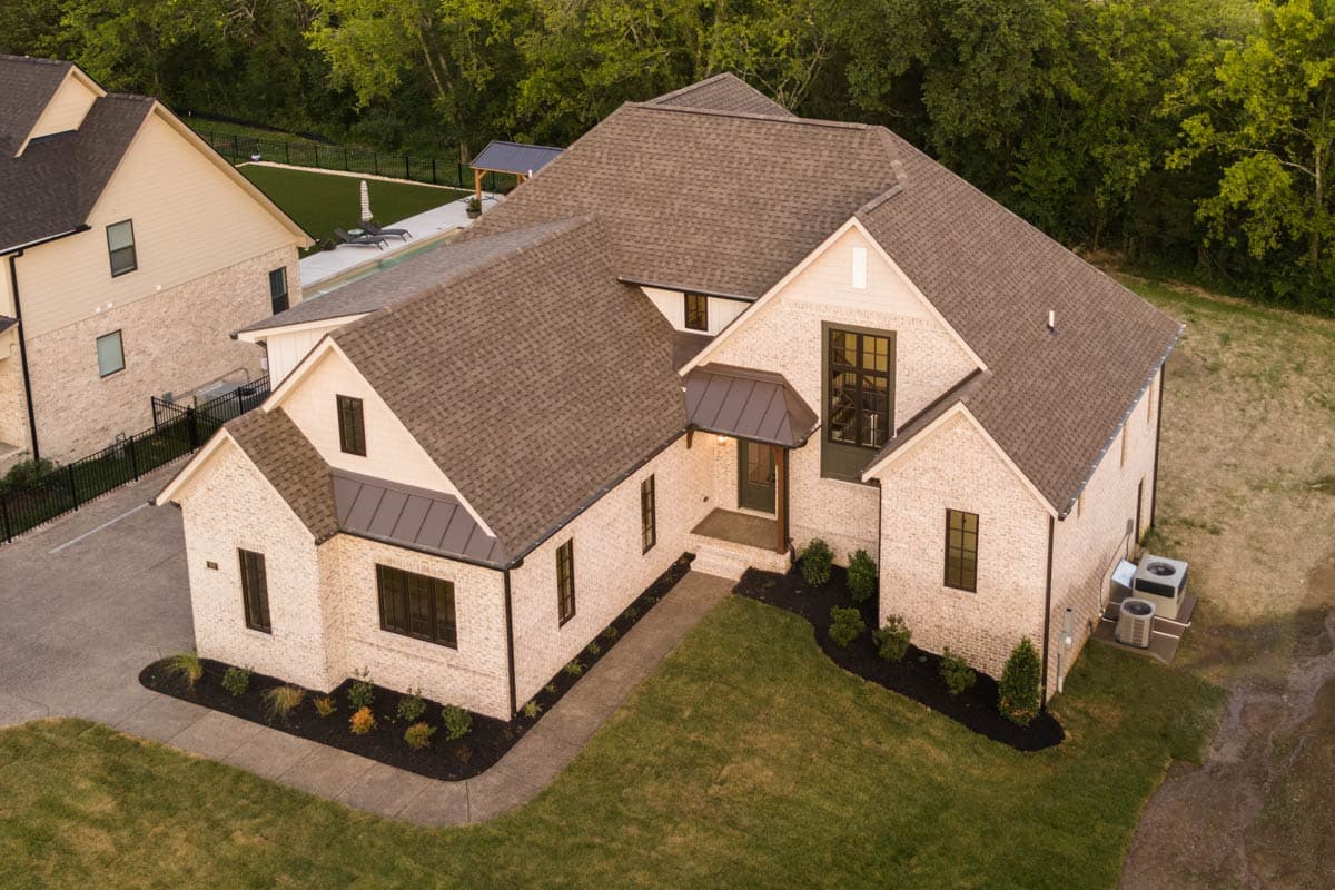 House plan exterior: Modern farmhouse style, two stories, brick facade, gabled roof, and covered front entrance with metal awning.
