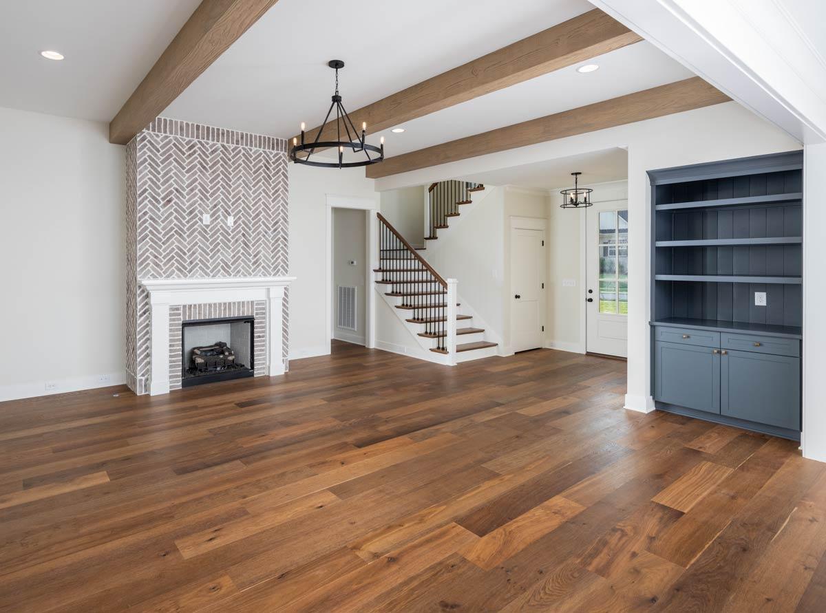 Interior view: Living area with fireplace, built-in shelving, wood beams on ceiling, and staircase to second level.