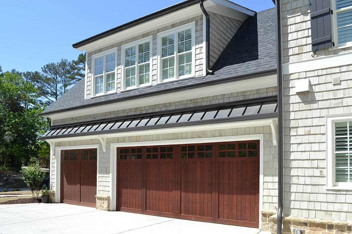 Exterior shot of a multi-car garage with dark wood doors and light gray shingled siding. Multiple windows above garage doors.
