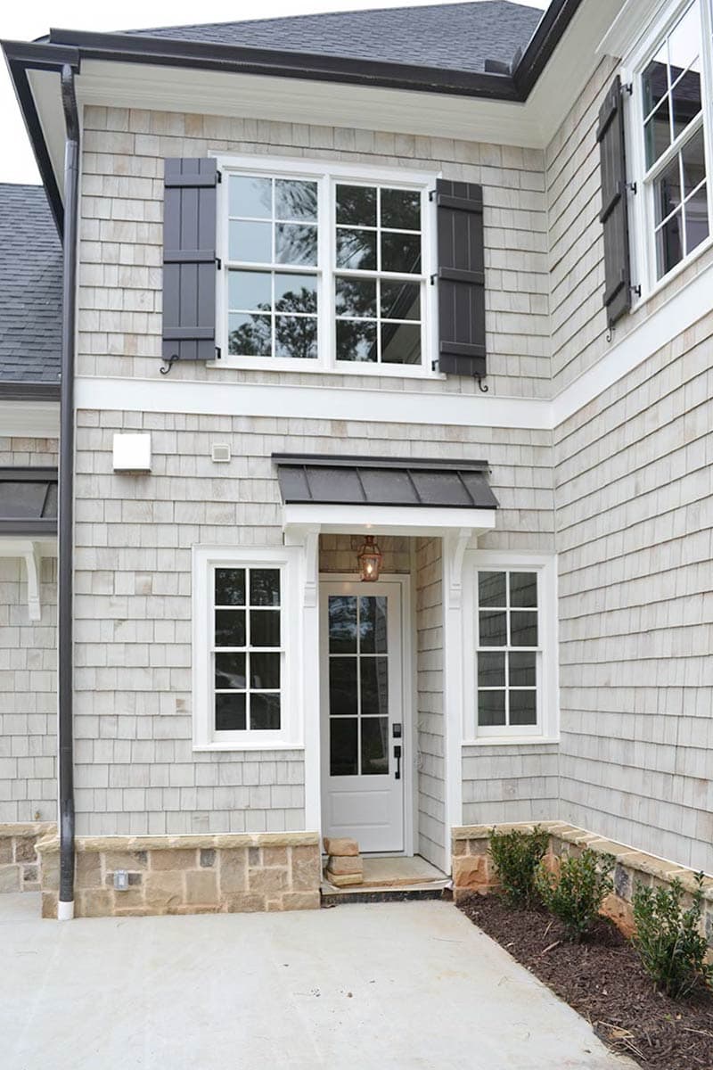 Exterior of a two-story house with gray shingle siding, white-framed windows, and a front door with a small awning.