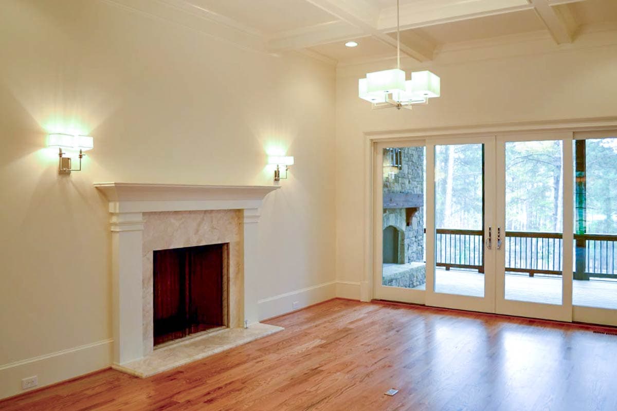 A bright living room with a fireplace, hardwood floors, and sliding glass doors leading to a forest view.