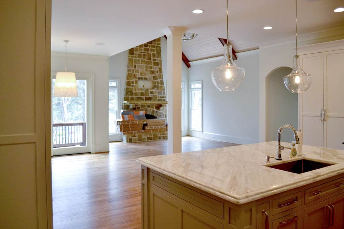 A newly renovated kitchen with a large island and two clear glass pendant lights. A stone fireplace is visible in the background.