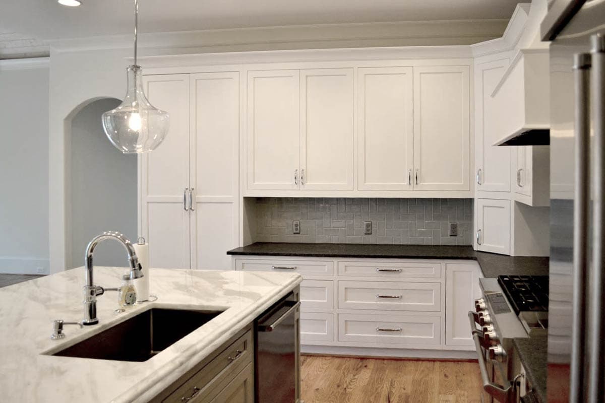 A modern kitchen with white cabinets, a marble countertop island, and a decorative glass pendant light. Appliances are stainless steel.