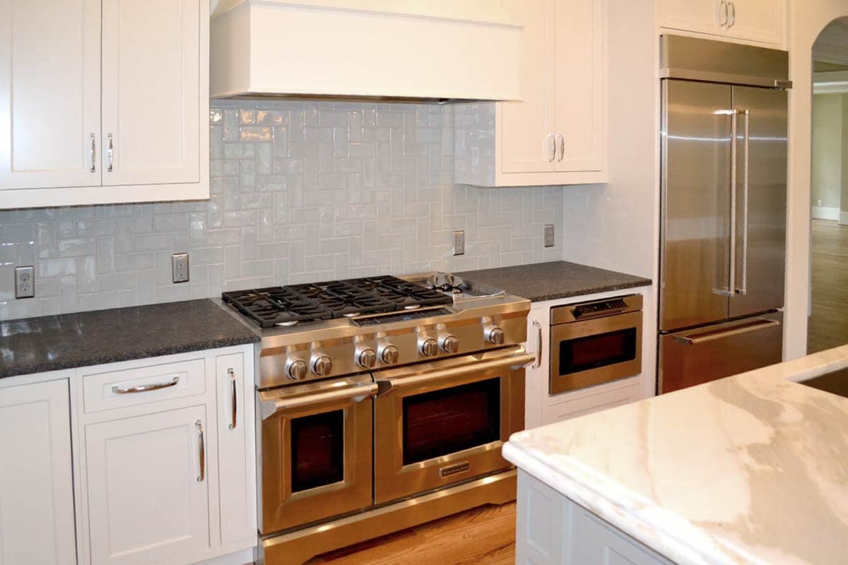A modern kitchen with stainless steel appliances, white cabinets, and a gray-tiled backsplash. Features include a large range and refrigerator.