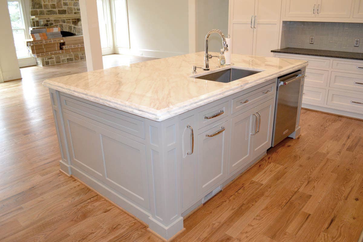 A newly built kitchen island with a marble countertop. The island has a sink, a dishwasher, and gray cabinet doors with silver handles.