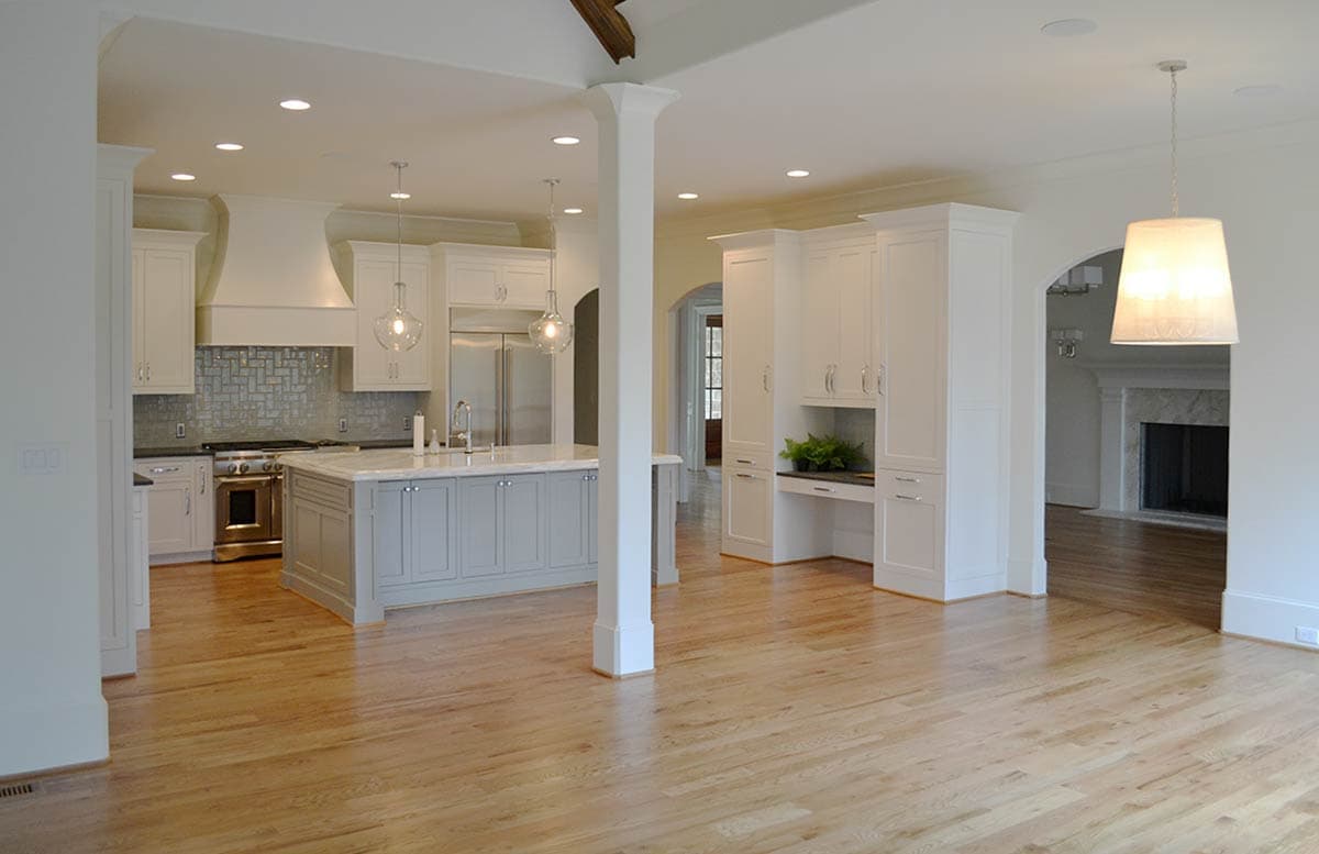 A spacious, modern kitchen with white cabinetry, a large island, stainless steel appliances, and hardwood floors. Pendant lights hang above.