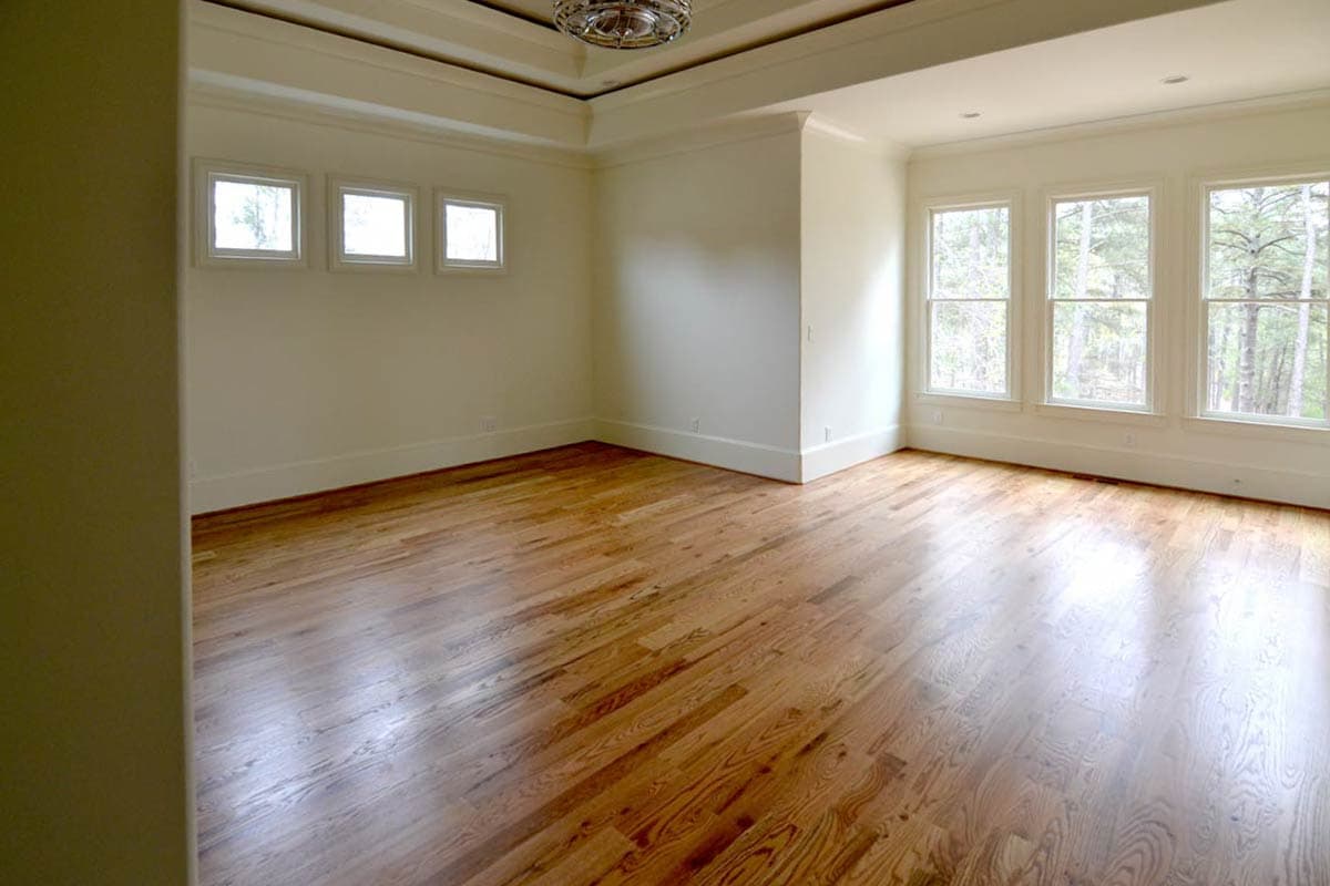 An empty room with light wood floors, three windows on the right wall and three on the left. The room is brightly lit.