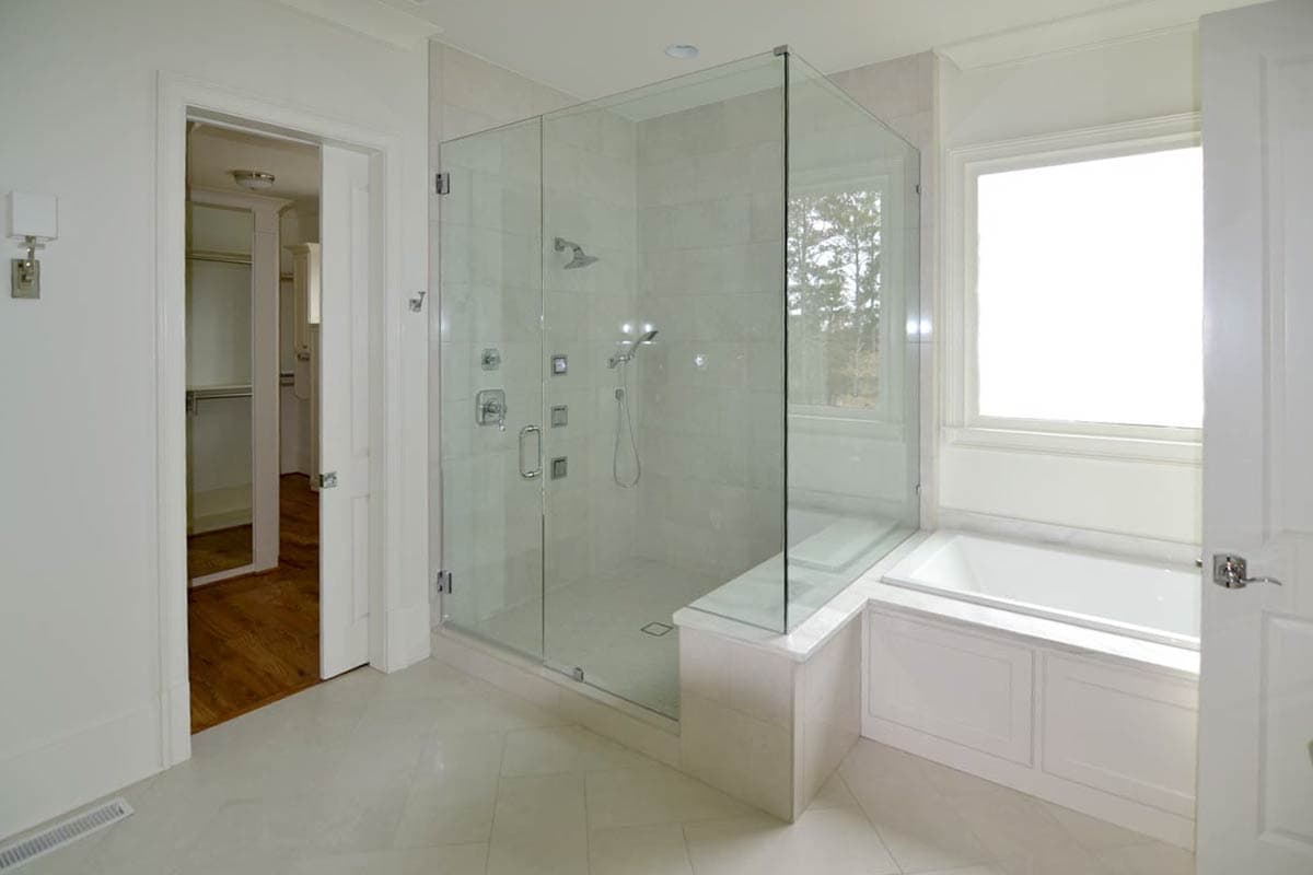 Spacious, modern bathroom featuring a walk-in glass shower, a soaking tub, and an open doorway leading to a walk-in closet.