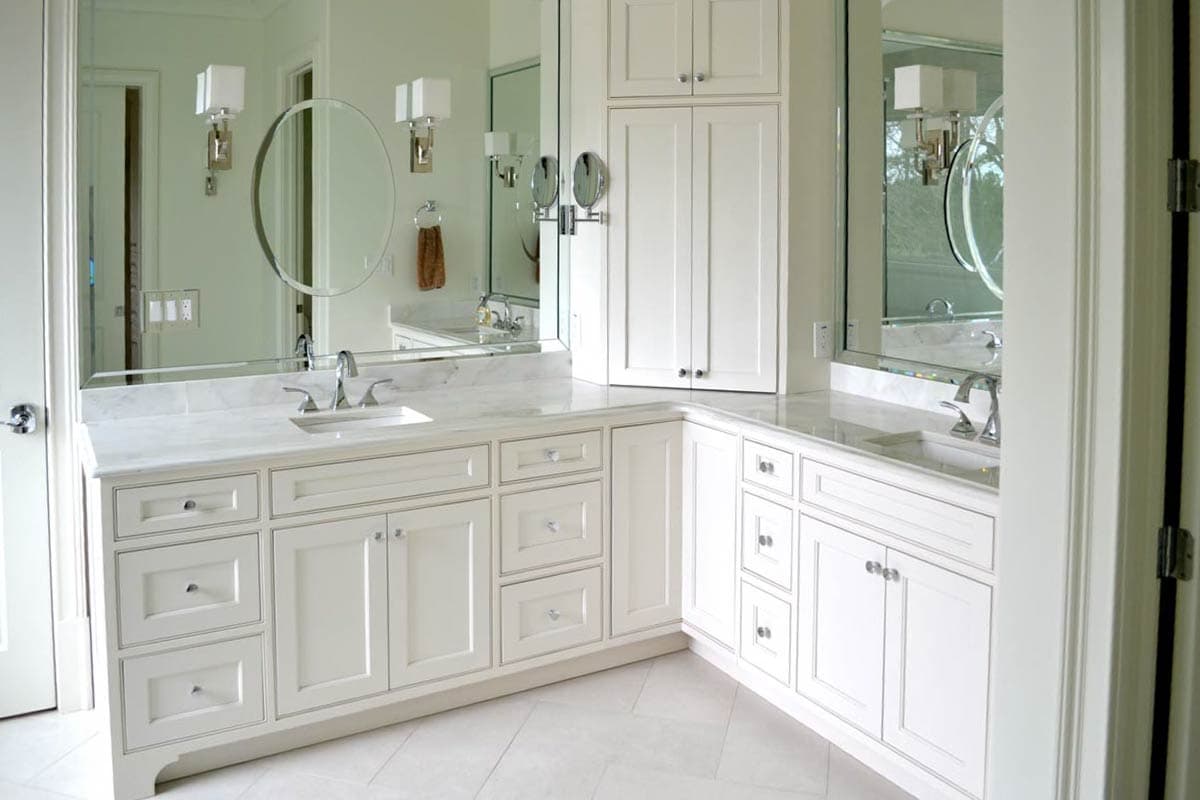 A luxurious white bathroom featuring a large mirror above a double vanity with two sinks. Elegant lighting and cabinetry.