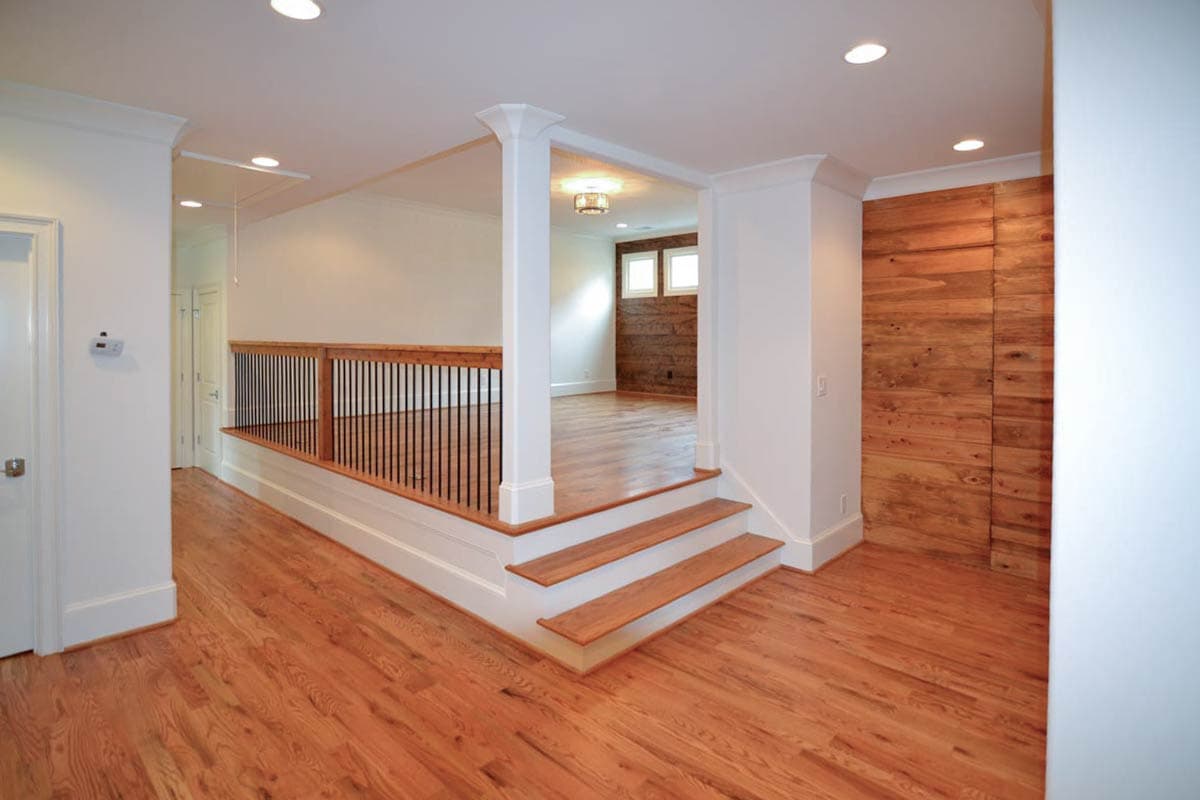 Brightly lit interior with hardwood floors. A raised area with a railing and steps leads to another room with wooden wall paneling.