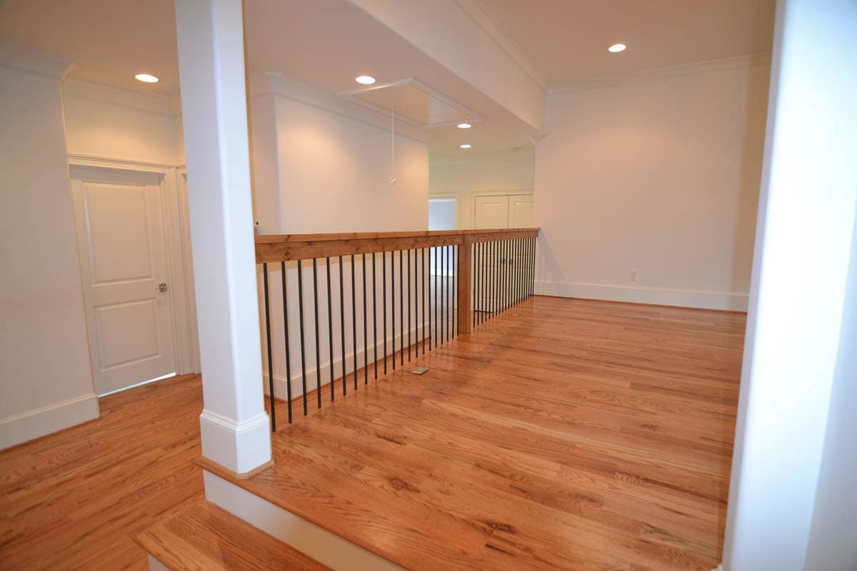 Interior shot of a well-lit home, featuring hardwood floors, a railing with dark spindles, and white walls with minimal decor.