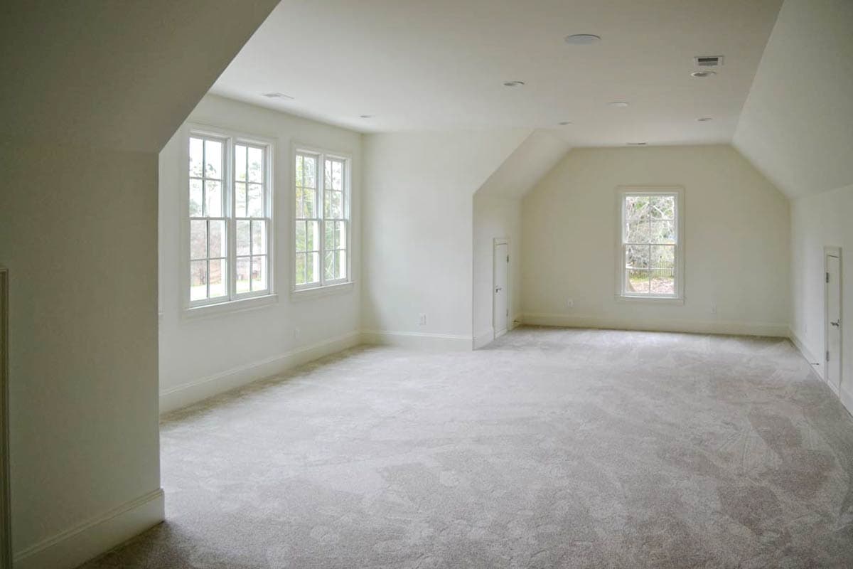 An empty, bright room with white walls, three windows and a single window, soft gray carpet, and multiple doors leading to other areas.