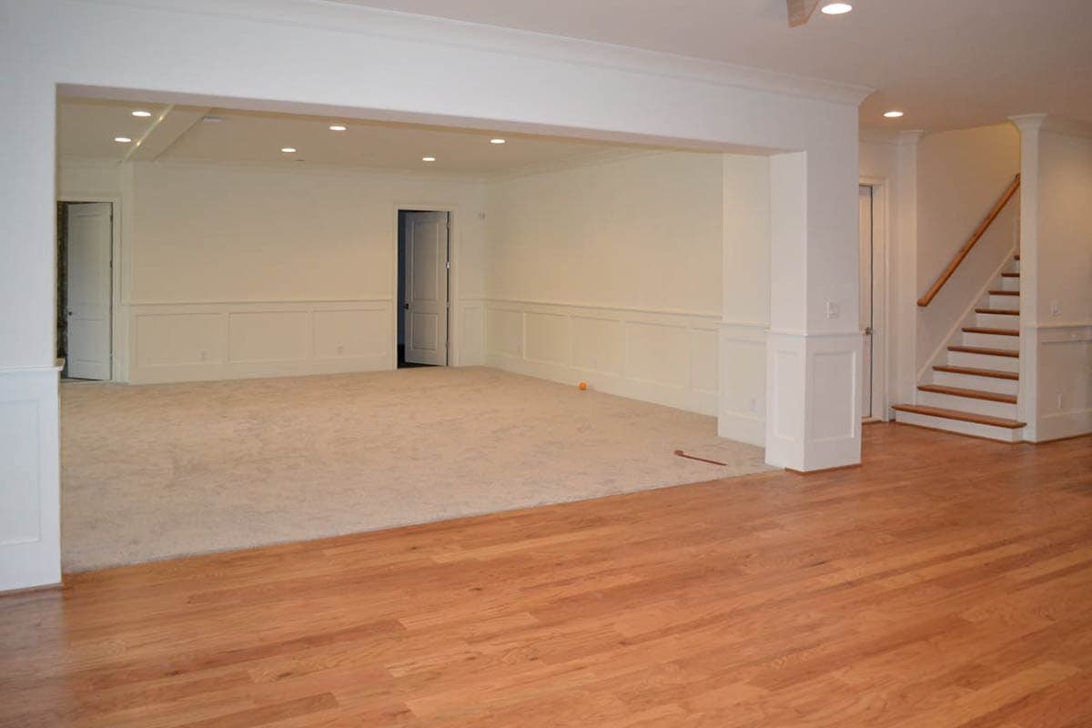 Spacious, newly built interior with light beige carpet and hardwood flooring. A staircase and several doorways are visible. 