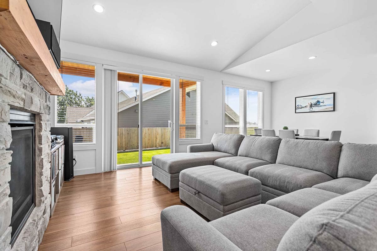 Living room with stone fireplace, large sectional sofa, and sliding glass doors opening to a backyard.