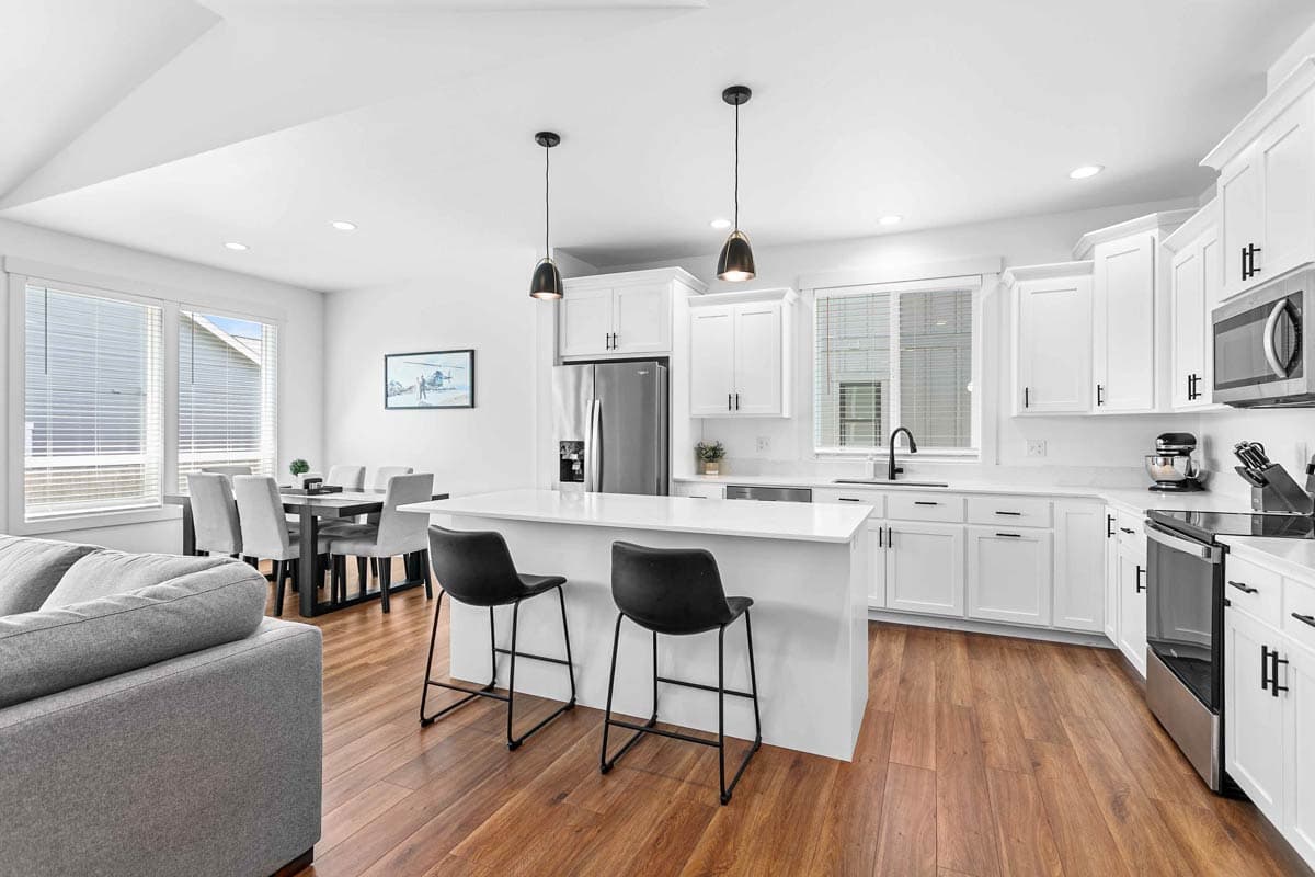 Open concept kitchen with white island and cabinets, stainless steel appliances, dining area, and living room seating.
