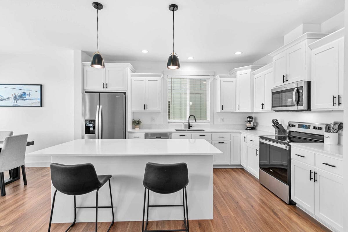 Modern kitchen with white cabinetry, island with seating, stainless steel appliances, and pendant lights.