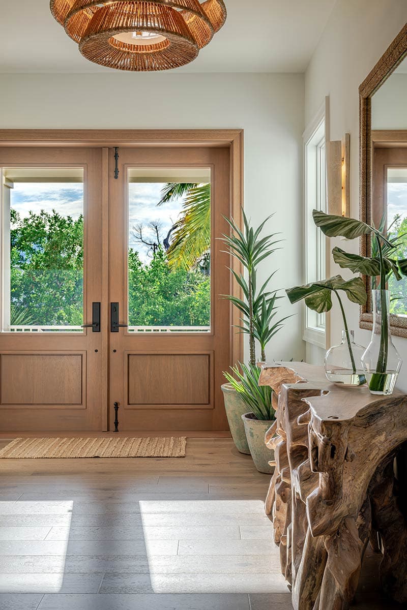 Bright, airy entryway featuring a wooden double door with a view of greenery, and a rustic wooden console table with plants.