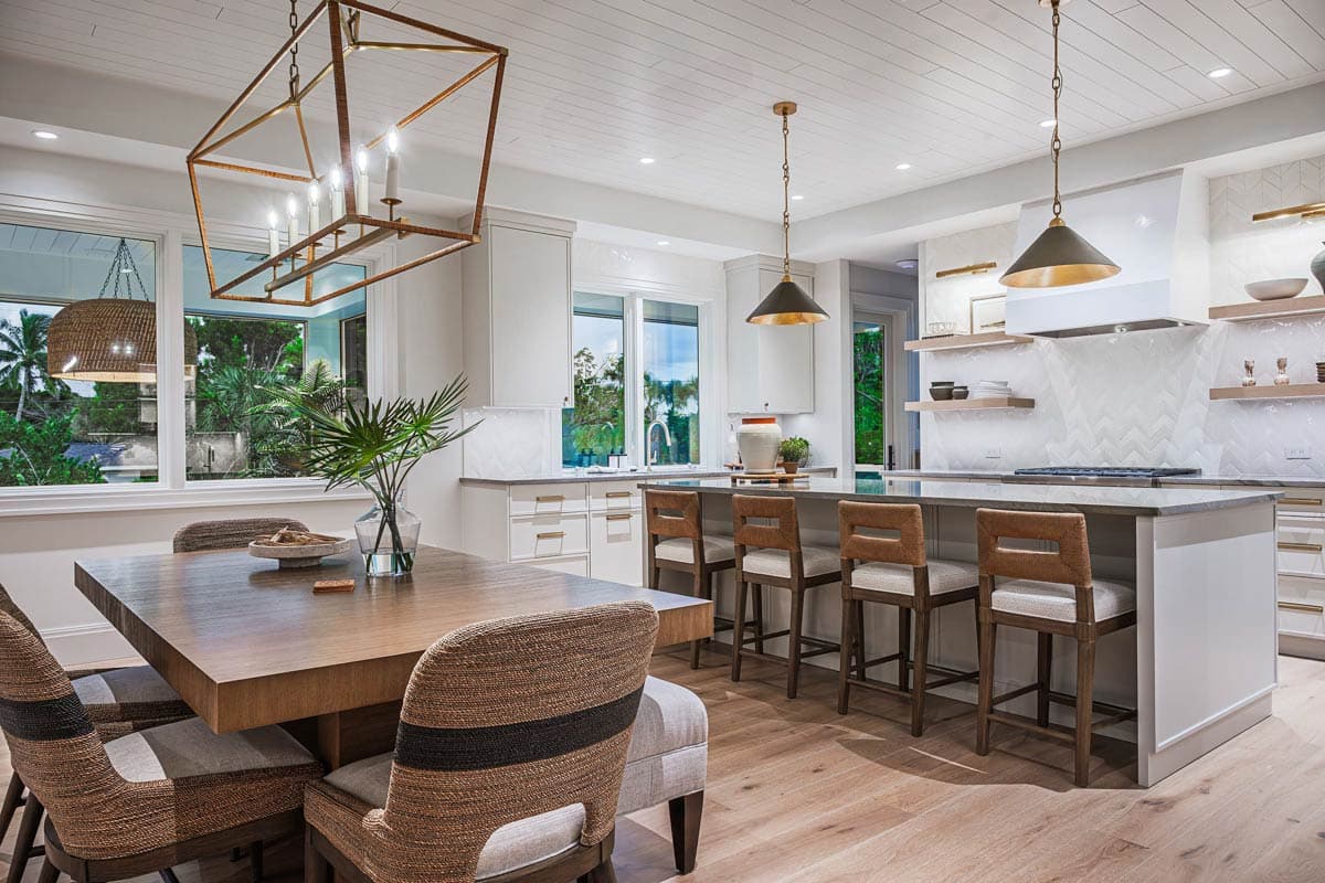 A modern kitchen and dining area features a large island with bar stools, a wooden table, and unique geometric light fixtures.