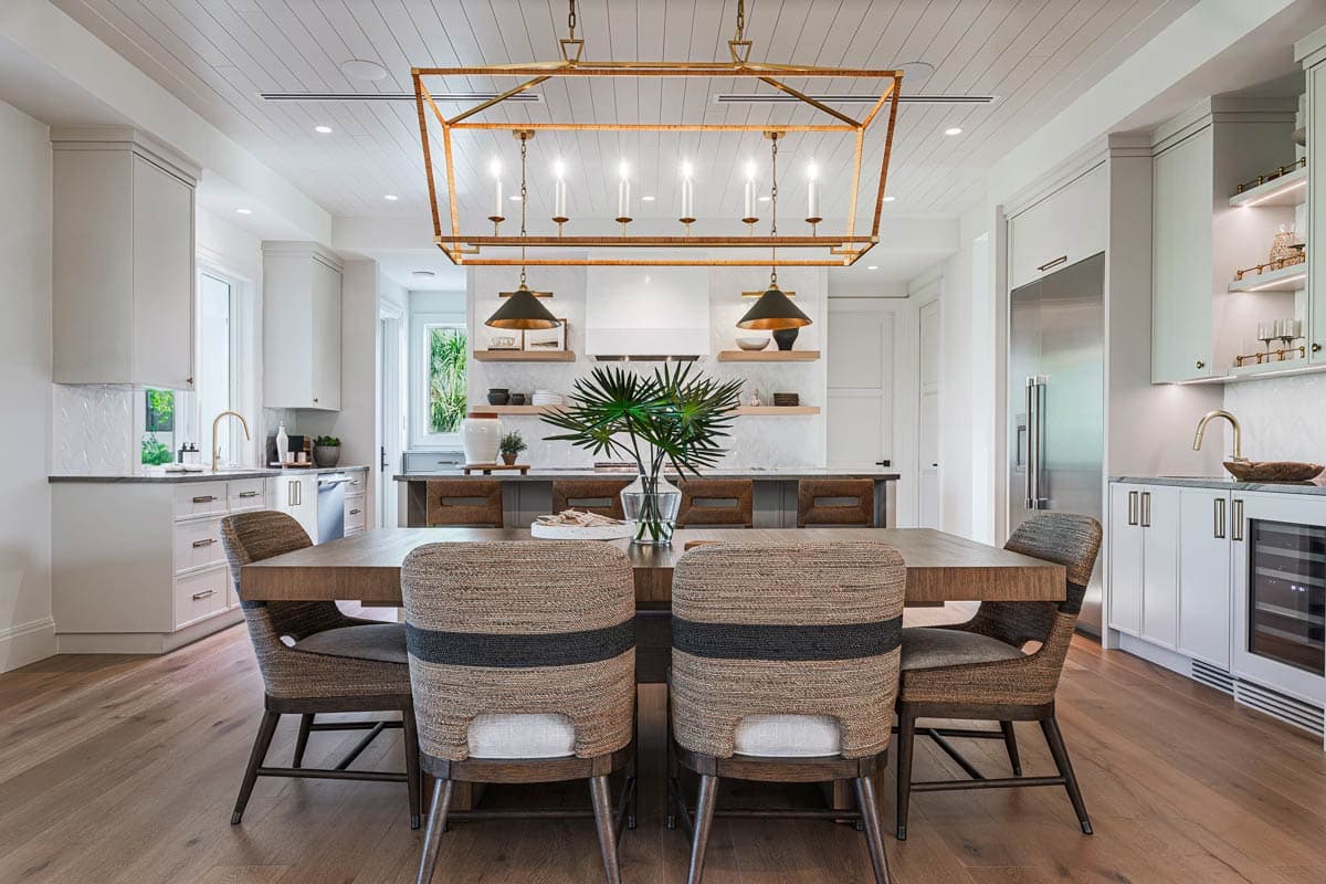 Formal dining room with a large wooden table and woven chairs beneath a geometric chandelier. The space is bright and airy.