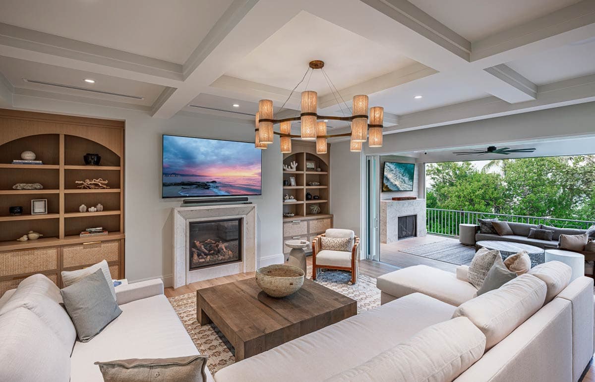 A luxurious living room features a fireplace, a large TV, and an outdoor patio with a matching fireplace.  A modern chandelier hangs overhead.