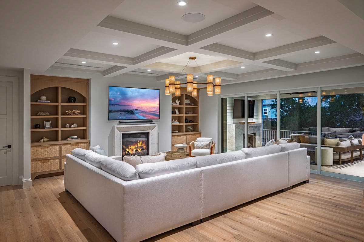 Living room with a large white sectional sofa, fireplace, and television. Natural light streams from the patio door and ceiling lights.