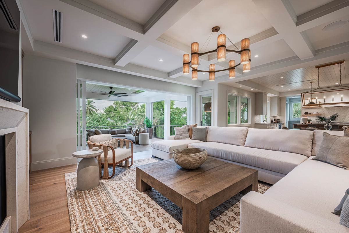 A luxurious living room features an open layout with an outdoor patio view. A large sectional sofa, wooden coffee table, and unique chandelier.