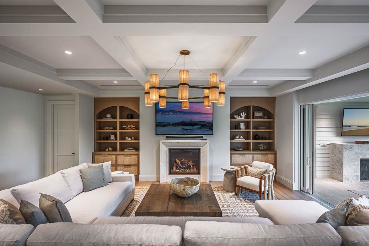 Living room with cozy neutral tones features a fireplace, TV, and light fixtures. A large sectional sofa faces a coffee table.