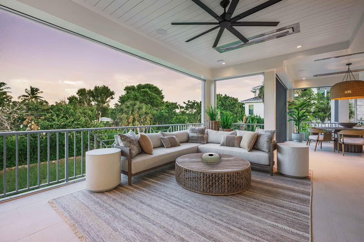 Spacious outdoor patio featuring a sectional sofa, coffee table, and area rug. Lush greenery surrounds the balcony with a view of trees.