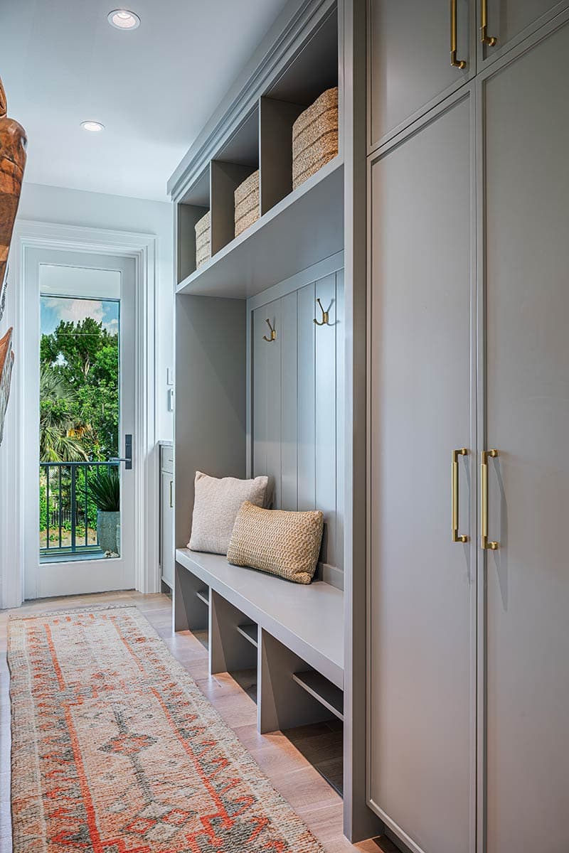 A well-lit hallway with a built-in bench, storage, and coat hooks. A door offers a view of greenery. An area rug adorns the floor.