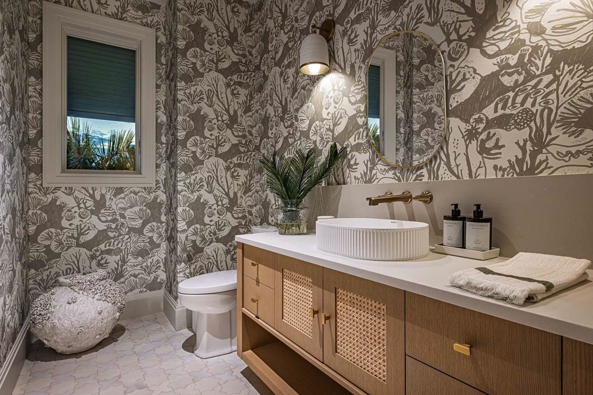 A powder room features botanical wallpaper, a modern wood vanity, and a circular mirror. A white, ribbed sink sits on the countertop.