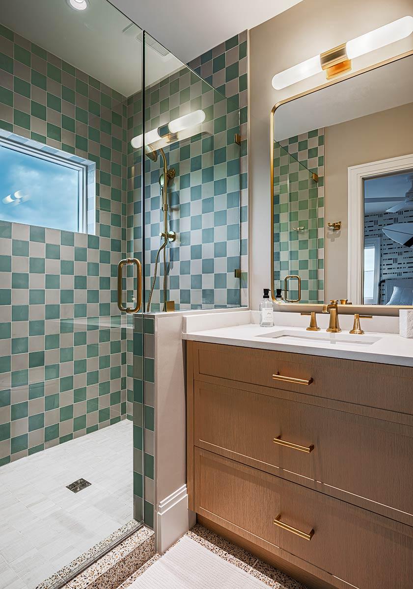 A modern bathroom showcases a tiled shower, a wooden vanity with gold hardware, and a large mirror with a built-in light fixture.