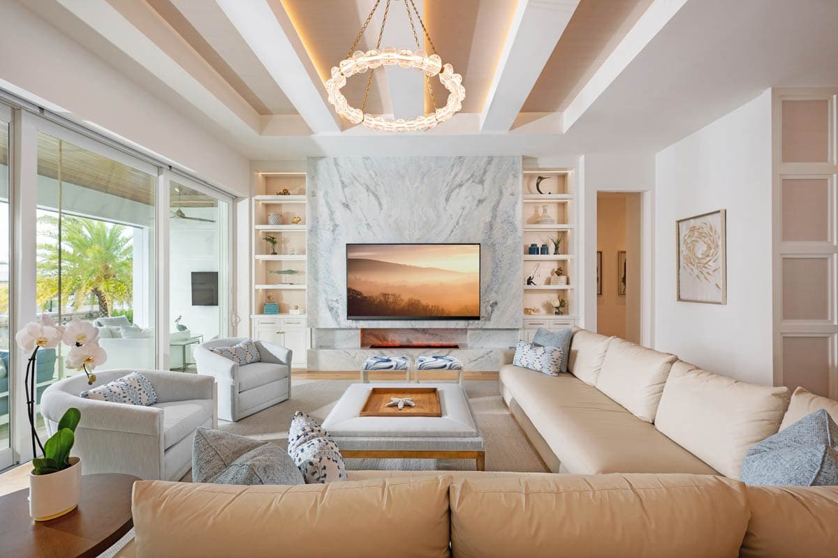 Living room with marble fireplace, built-in shelving, coffered ceiling, and large sliding glass doors leading outdoors.