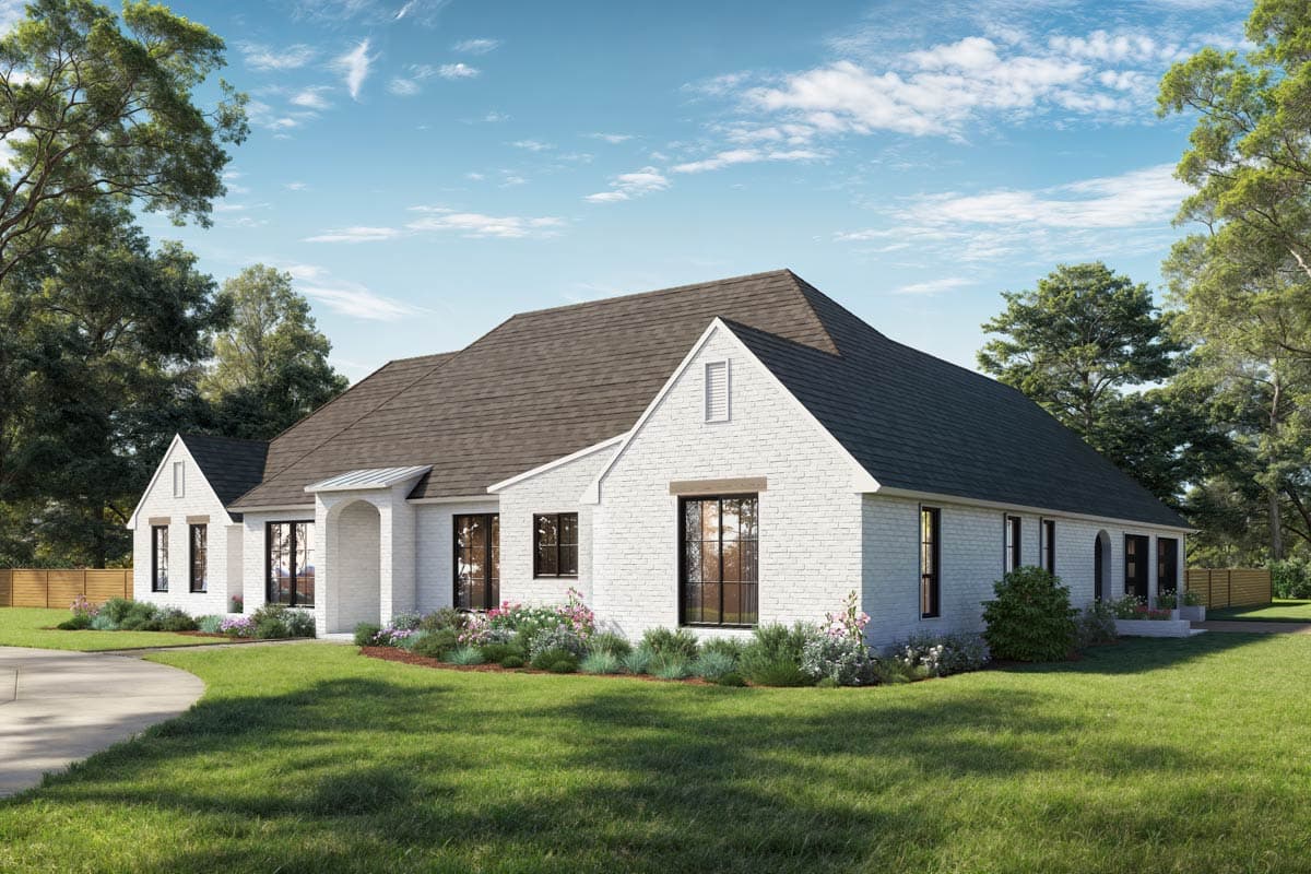 A white brick house with a brown roof and black-framed windows, surrounded by green grass and trees under a blue sky.