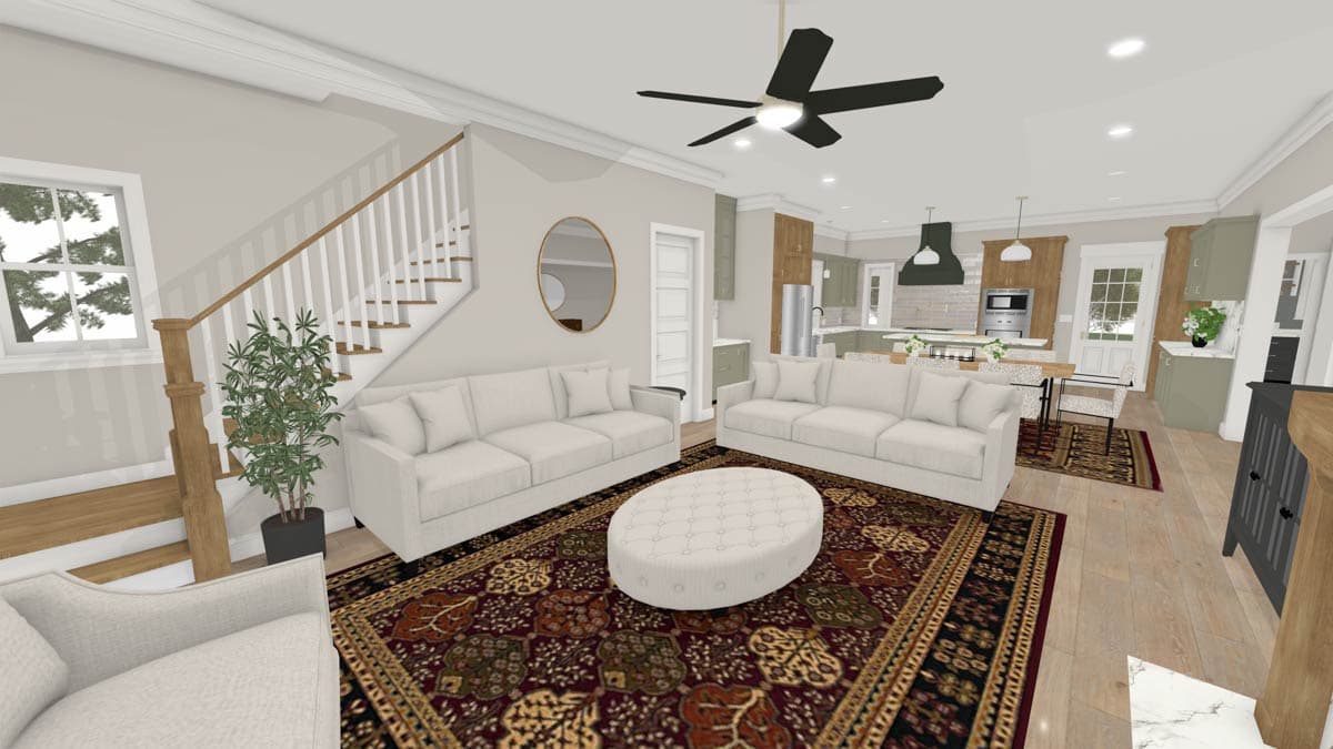 A modern open-plan living space with a kitchen, two white sofas on a patterned rug, a staircase, and a large ceiling fan.
