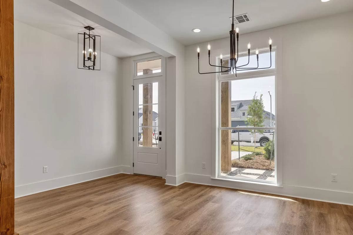 Interior view of a room with wood-look flooring, large windows, a glass-paneled door, and two modern chandeliers.