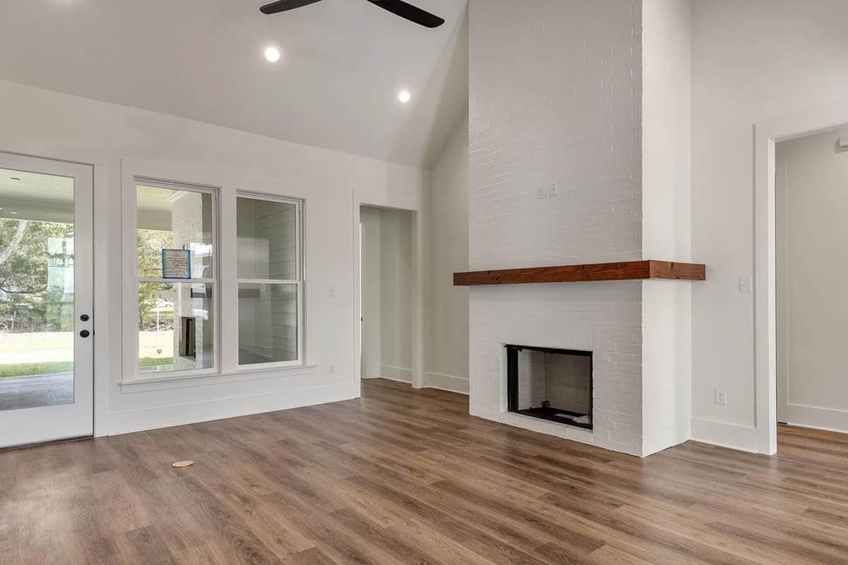 Interior view of a room with white brick fireplace, wooden mantel, vaulted ceiling with fan, and glass door.