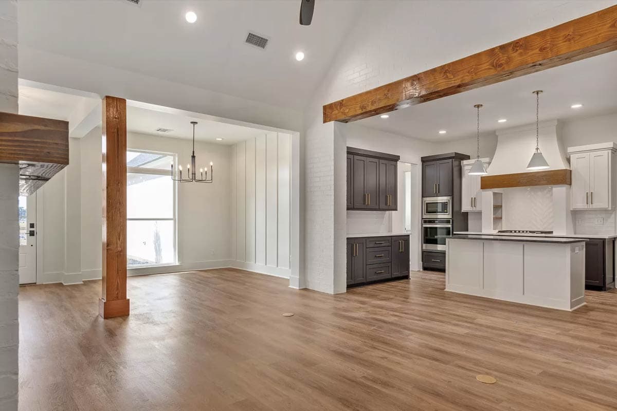 Open concept living area with vaulted ceiling, exposed wood beam, kitchen island with pendant lights, and a dining area.