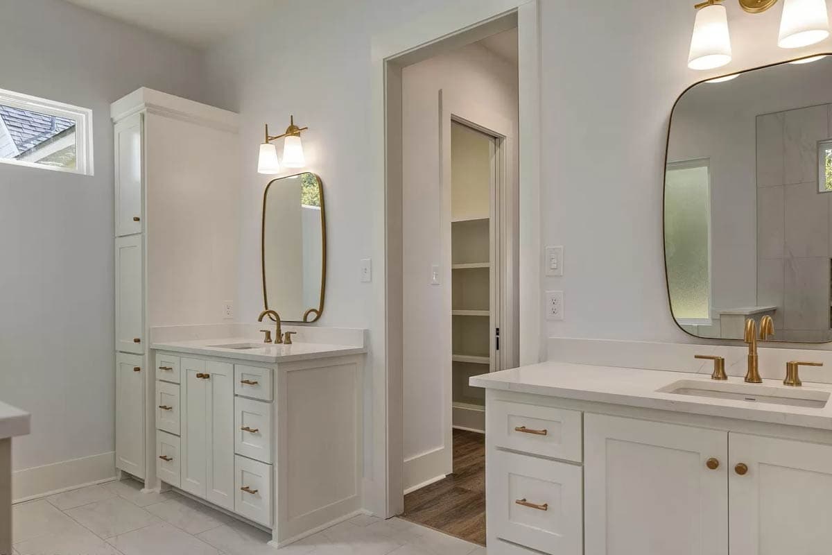 Modern bathroom with double vanities, brass fixtures, and a walk-in closet. White cabinets and countertops.