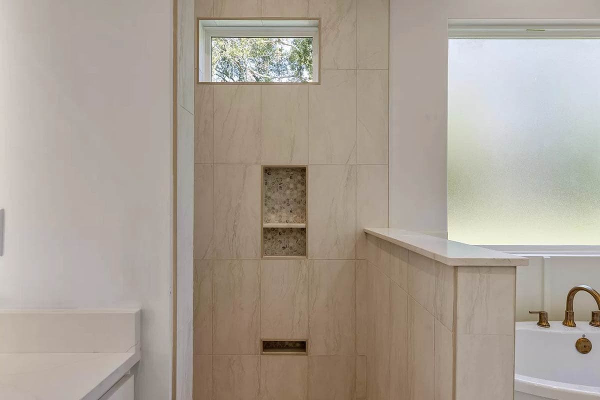 Bathroom with tiled shower featuring recessed niches and a horizontal window above. Bathtub visible with brass fixtures.