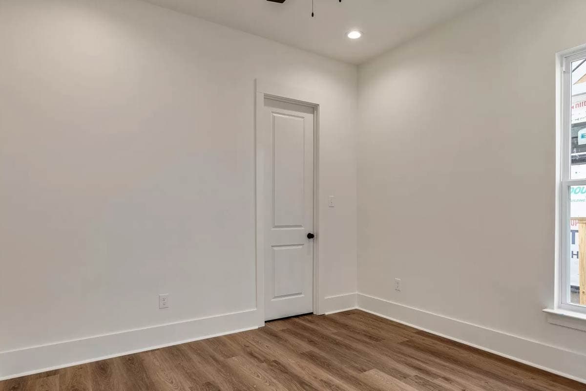 Interior view of a room with white walls, a white paneled door, and wood-look flooring.