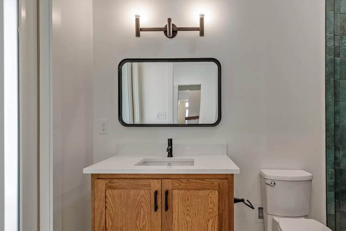 Bathroom interior featuring wood vanity, quartz countertop, rectangular mirror, modern sconce, and white toilet.